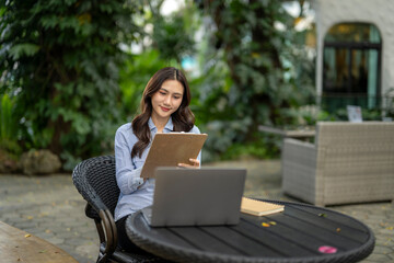 Asian woman working remotely on laptop with a clipboard