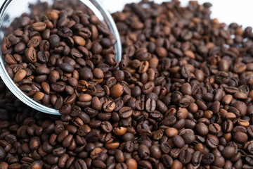 Obraz premium Roasted coffee beans spilling from glass bowl