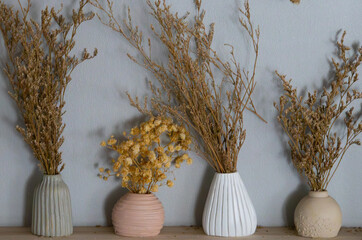 Minimalist dried flower arrangement in small ceramic vases on wooden shelf