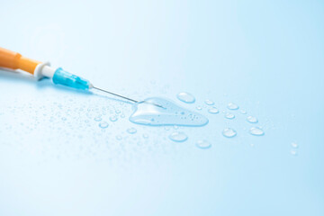 Dropper needle lies in drop of medicine on blue background.