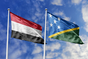 Waving flags of the Yemen and Solomon Islands together on blue sky background. Official diplomatic relations, partnership and business concept.
