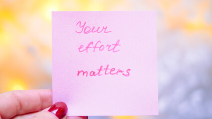 Hand holding pink sticky note with motivational quote about effort