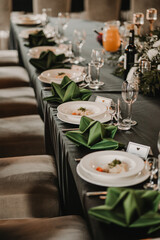 Fototapeta premium Elegant wedding reception table with plates, crystal glasses and folded green napkins prepared for formal celebration. Luxury banquet setup for romantic wedding dinner, fine dining event and festive h
