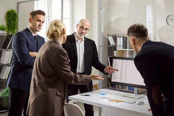Business meeting analysis with team colleagues. A businessman gives a presentation at a computer as a businesswoman and colleagues discuss data in an office. Clear teamwork and analysis concept.