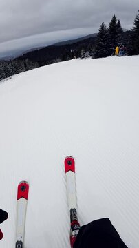 Travel and winter adventure concept. Beautiful POV ski landscape on the mountains. Skier skis down a snowy mountain trail in cloudy weather. Vertical shot