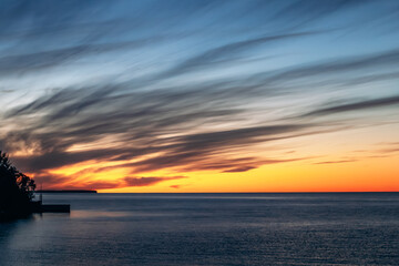Dramatic sunset over a large body of water with intense orange horizon and sweeping blue clouds at dusk, Le Domaine-du-Roy, Quebec, Canada