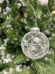 christmas tree decoration, Close-up of a transparent glass Christmas ornament hanging on a green fir tree branch. Delicate white decorative lines and glitter details on the bauble