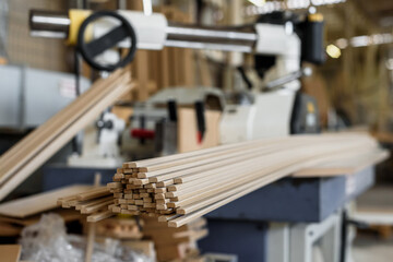 Warehouse with wooden blanks for doors production at manufacturing plant. Pile of thin wooden slats near industrial machine at door production plant
