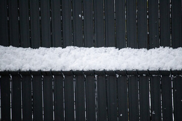 Horizontal line of white snow accumulating on black vertical garden fence slats