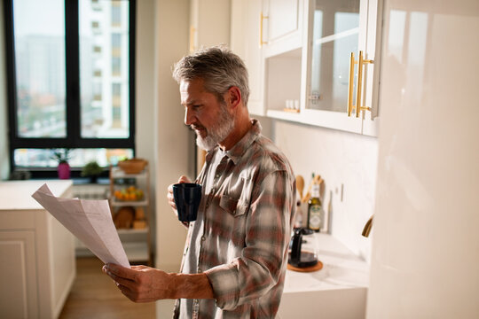 Mature man reading mail with coffee in home kitchen, thoughtful