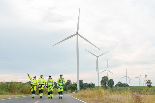 Caucasian adult engineer team walking rural road beside wind turbine safety uniform teamwork inspection for renewable electricity generation clean power green technology outdoor maintenance