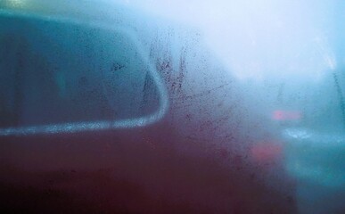 Abstraktes Motiv mit beschlagener Glasscheibe vor parkendem roten Auto bei Frost und K&auml;lte am Nachmittag im Winter