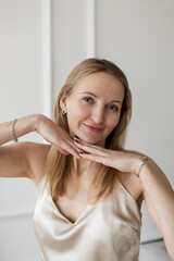 Smiling elegant woman in silk top posing indoors with hands under chin