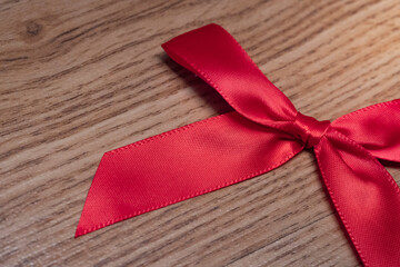 Elegant red satin ribbon tied into a neat bow on natural wooden background. Perfect for gift wrapping, holiday promotions, love themes, weddings, celebrations and marketing designs.