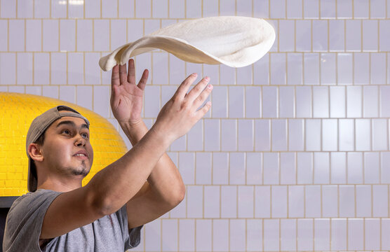 Pizza maker spinning dough in kitchen. Pizza chef makes the pizza dough spin in the air to make it thin and soft. Copy space