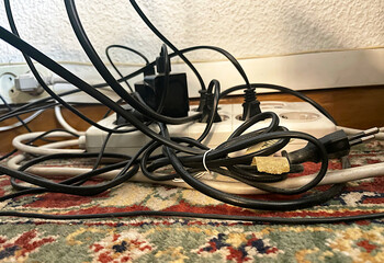 Cables el&eacute;ctricos enredados y enchufados a red corriente con ladr&oacute;n y regleta