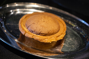 A freshly baked, round, brown pastry sits in the center of a shiny, oval silver tray, displaying its crisp texture, inviting colors, and intricate details under bright lighting