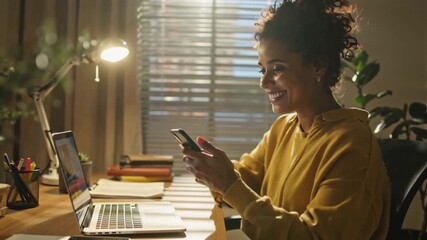 Rear view mixed-race woman sitting home desk, smartphone while working, glowing futuristic holographic interfaces digital charts floating cozy modern home office background cinematic 4K tech video - Powered by Adobe