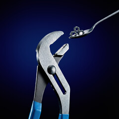 Conceptual studio shot of adjustable pliers opening jaws to receive hex nuts from a spoon like a hungry baby.