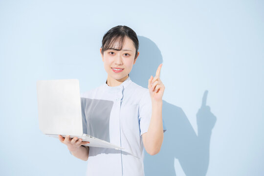 水色背景でパソコンを持つポイントやオススメの案内ポーズの女性看護師カメラ目線　転職や採用などのイメージ