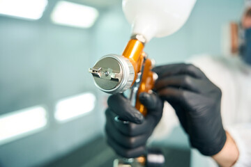 Automobile painter standing in paint chamber workshop holding painting gun