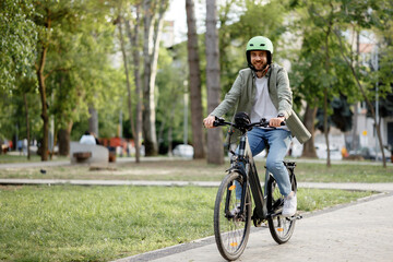 Naklejka premium Man rides bicycle in park wearing green helmet during daytime with trees and grass in view
