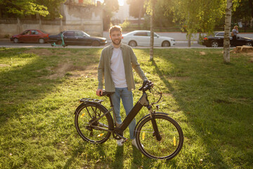 Man stands next to bicycle in park during sunset with cars in the background