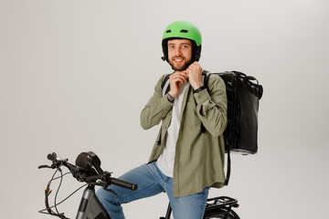 Young man with green helmet and backpack sitting on electric bike ready for delivery in bright indoor space