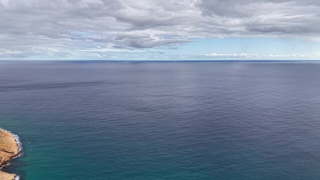 Expansive view calm open ocean and distant horizon under layered cloudscape, glassy water with gentle ripples,