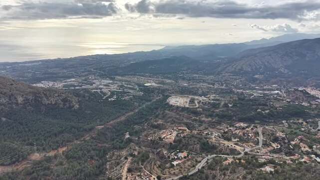 coastal valley overlook with sea, reflective water glinting under soft clouds, rolling hills, scattered villas