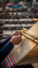 Person weaving on a loom with colorful threads outdoors.
