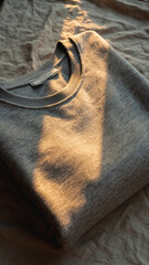 Folded gray sweatshirt on a textured surface, illuminated by warm sunlight.
