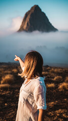 Person pointing at a mountain peak surrounded by clouds and mist.