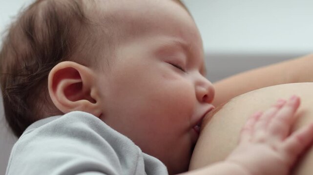 A young woman, who has recently become a mother, breastfeeds her baby while standing by the window