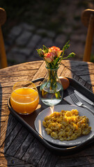 Breakfast setup with flowers, scrambled eggs, orange juice, and an egg on a tray.
