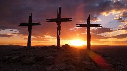 Three crosses on a rocky hill with sunbeams visible through clouds at sunset, depicting calvary during Good Friday or Easter.