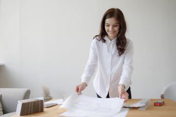 Young woman working on designs at a wooden table in a bright room during daytime with a focused expression on her face