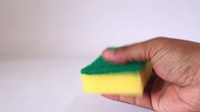 A hand (holding) squeezing a yellow green dishwashing sponge isolated