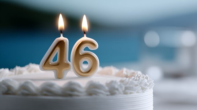 46th birthday cake with gold number 46 candles burning on white buttercream frosting with soft blue bokeh background