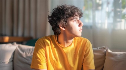 Man sitting on couch, looking off into distance with contemplative expression.