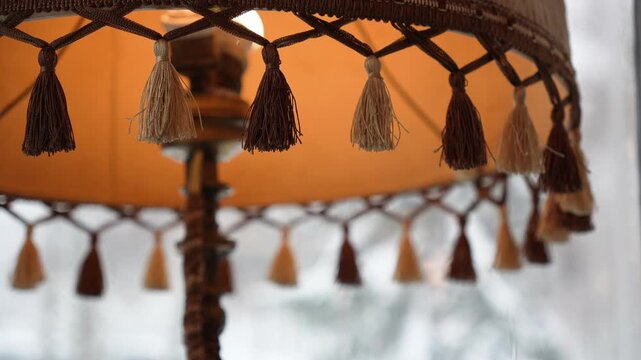 Decorative Fringed Lampshade with Small Hanging Tassels in Earthy Tones, Antique Style Table Lamp in a Warm Room Setting, Cozy Household Decor and Traditional Lighting Design