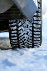 Close-up of car winter tire with snow on a frozen road