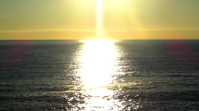 Golden sun path reflecting on a calm ocean surface at sunset with a small boat in the distance.