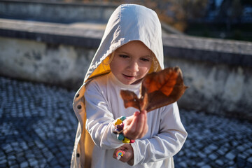 Curious child exploring nature details and studying a fallen leaf, autumn lifestyle concept.