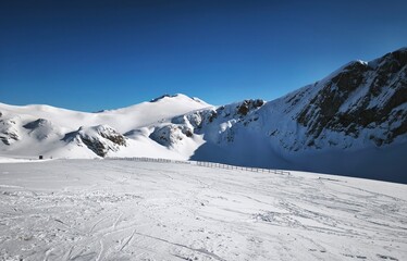 Snow-covered alpine plateau with mountains and wooden fence under blue sky