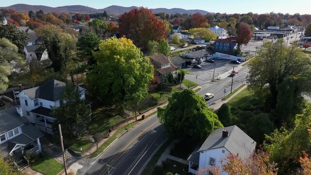 Aerial tracking shot of yellow school bus on street between colored trees in suburb housing area. Wide shot. Houses and homes in small town of USA.