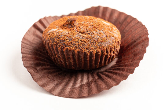 A freshly baked chocolate muffin with a dusting of cocoa powder is presented on a brown paper liner