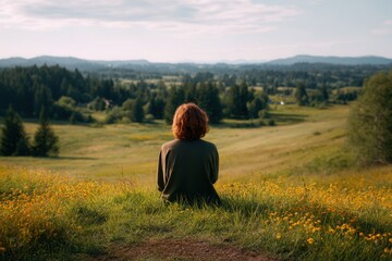 Serene Moment: Individual Sitting on a Small Hill Overlooking a Beautiful Nature Landscape with Fields and Mountains
