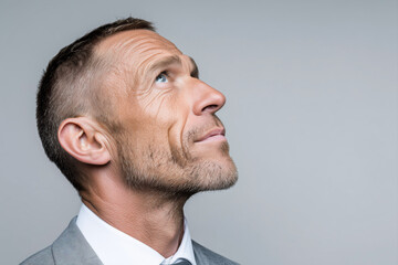 Obraz premium Thoughtful mature European business man executive in side profile looking up against light background. Serious professional male leader reflecting on life crossroads career decision and future