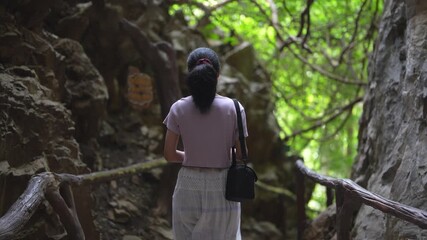 Sustainable eco-friendly travel concept. Light at the end of the tunnel: A young woman discovering a beautiful forest from a cave exit.